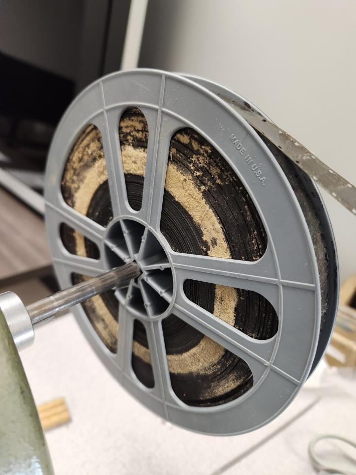A gray plastic film reel holding a roll of 8mm film with visible dust and debris.