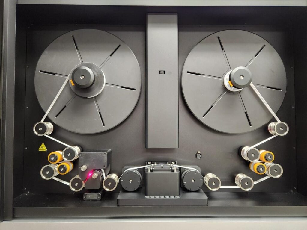 A professional film scanner with two large circular reels and a complex path of rollers and guide pins.