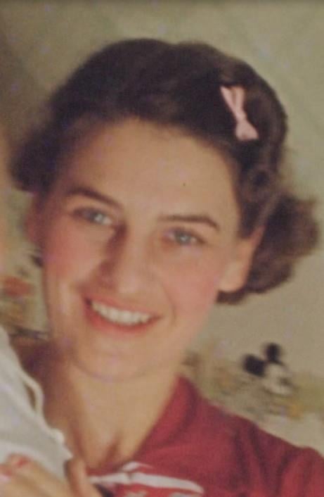 A portrait of a smiling woman with her hair styled in a side bun accented by a small pink bow.